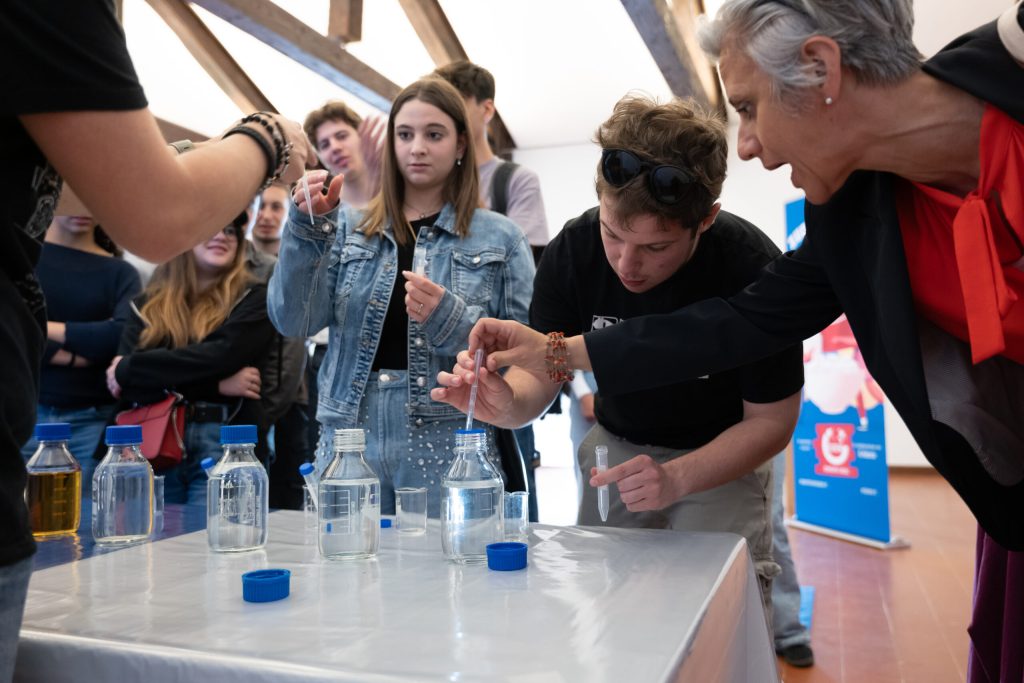 Studenti delle superiori attorno al banco durante un laboratorio Ossigeno, mentre travasano un liquido in una provetta