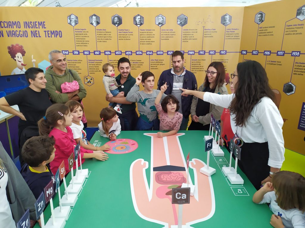Un'animatrice spiega il gioco degli elementi a un gruppo di bambini e adulti