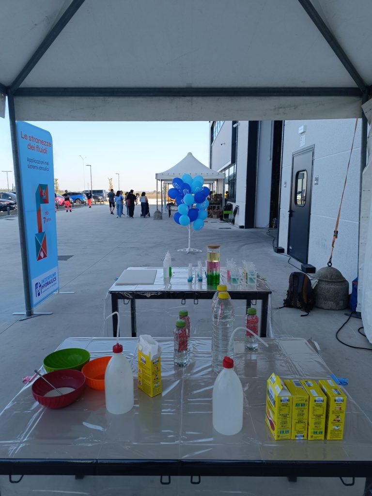 Il tavolo degli esperimenti sotto il gazebo, con il viale dell'open day sullo sfondo