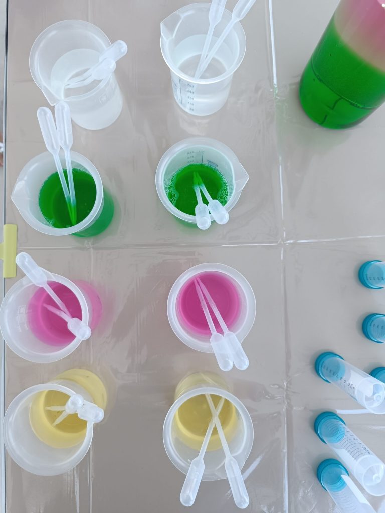 Bicchierini con liquidi verdi, rosa e gialli allineati per l'esperimento sui colori