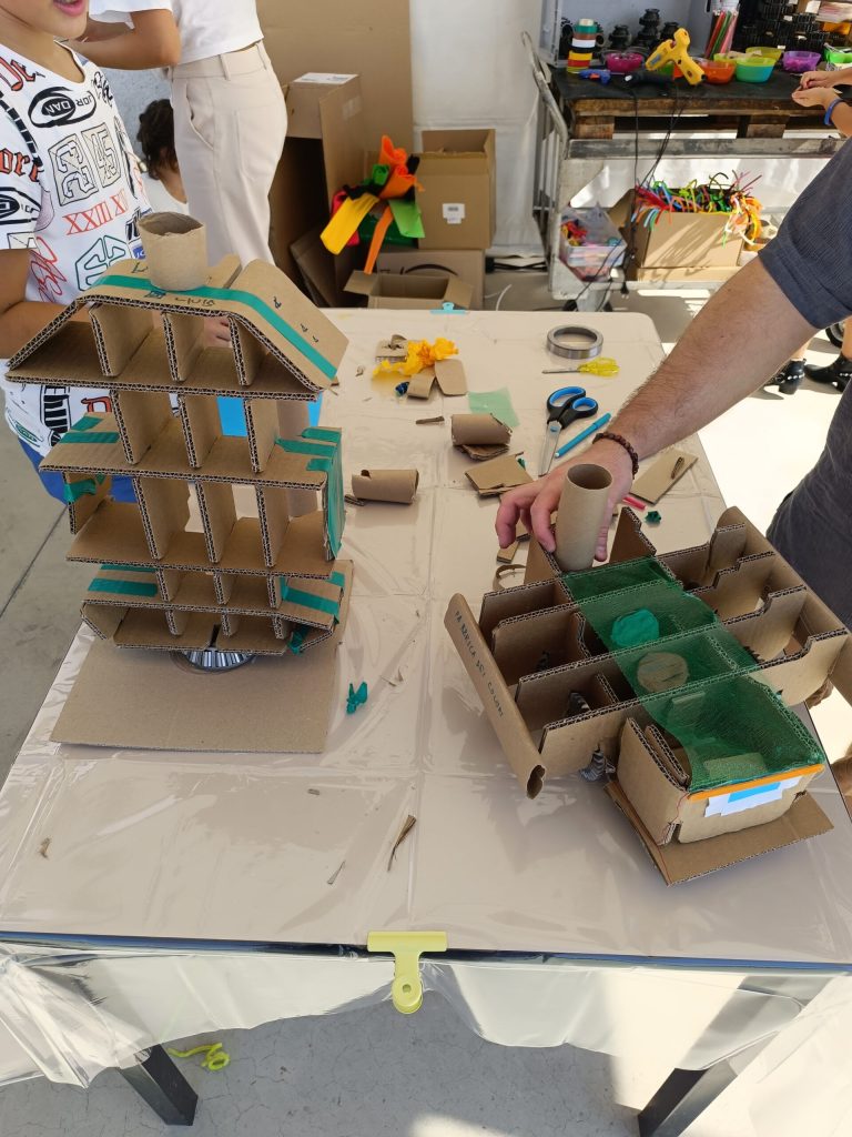 Mani di bambini che assemblano modellini di cartone al tavolo del laboratorio