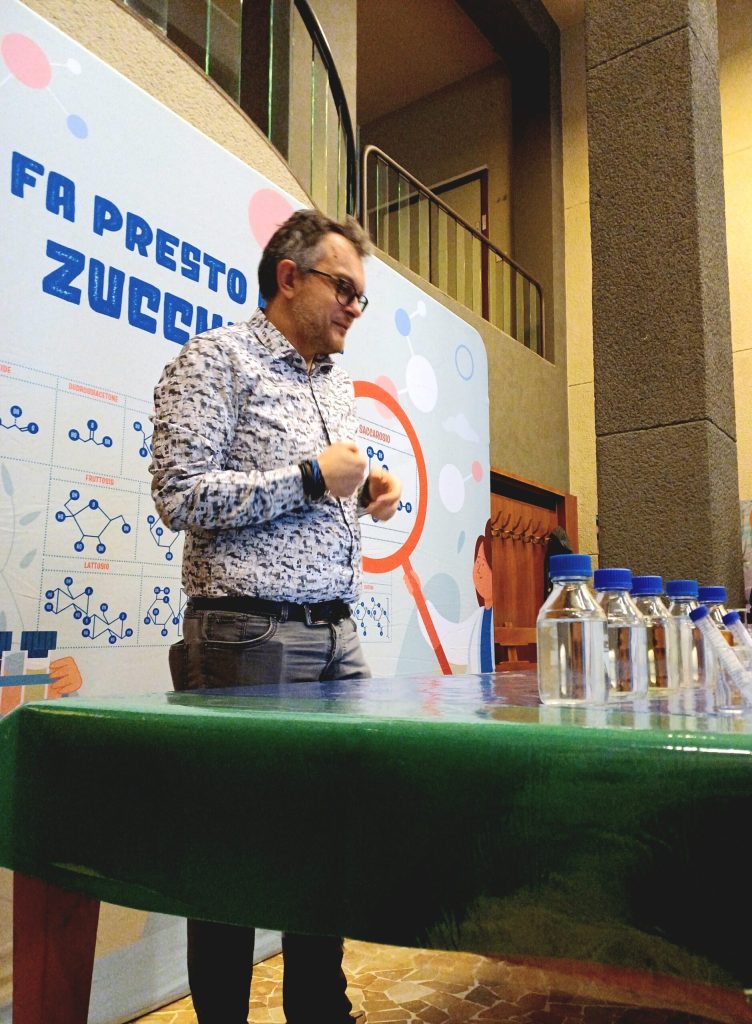 Un divulgatore parla al pubblico davanti al pannello di Zucchero & Co.