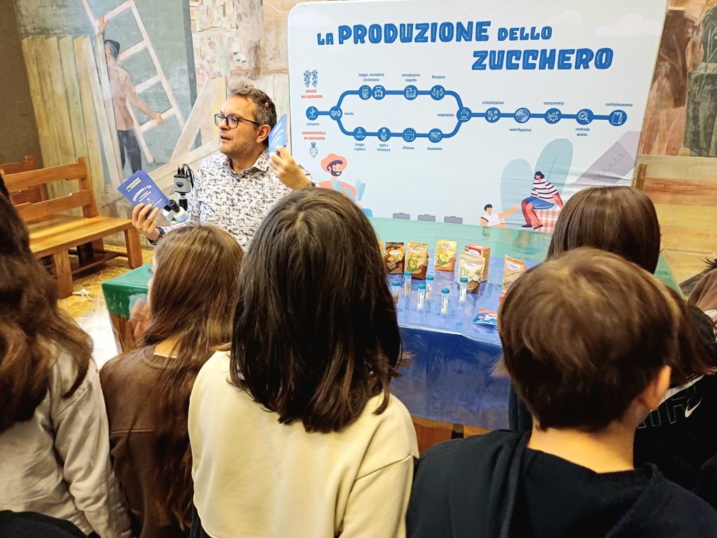 Un divulgatore racconta la produzione dello zucchero a un gruppo di bambini di spalle