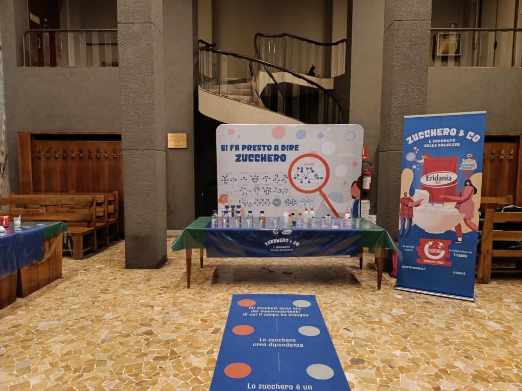 Il banco del laboratorio e il roll-up di Zucchero & Co. nell'atrio del festival