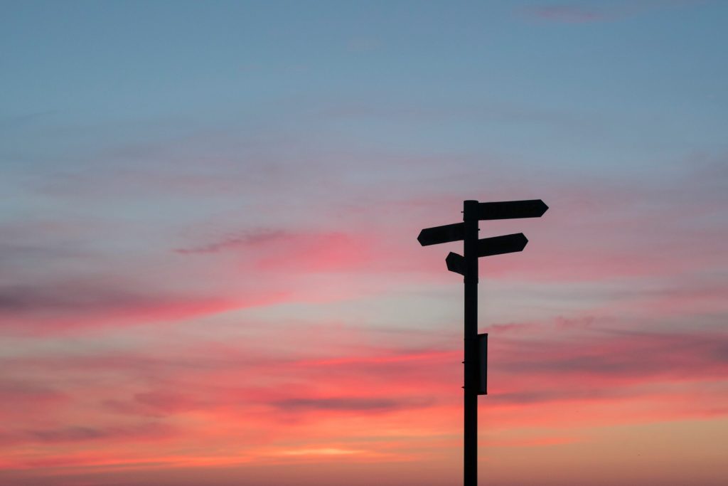 Un palo con pi&ugrave; cartelli indicatori rivolti in direzioni diverse, contro un cielo al tramonto